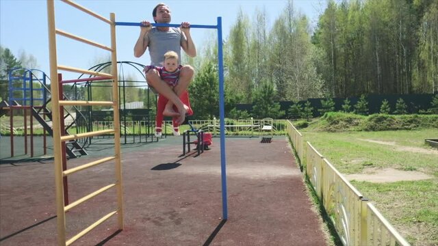 Family work out. Young man does pull ups with his baby. Adult male performs work out with his little child as additional weight.