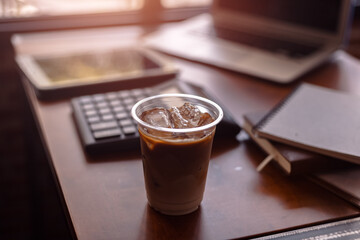 Ice coffee on office workplace with laptop, calculator, book and document on wood table