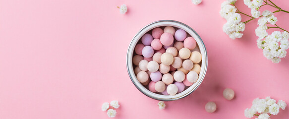Pearl make up powder with white flowers on pink pastel background. Copy space. Top view.