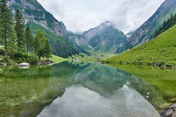 Naklejka na ściany i meble Landscape panorama from Seealpsee, Alpstein range of the canton of Appenzell, Switzerland. Green nature, mountains and their reflections on the lake.