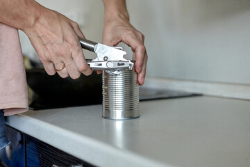 A woman in the kitchen opens a can. Hand open canned food in metal can. Close up canned goods non...