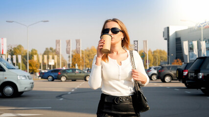 Portrait of stylish blonde woman drinking coffee on car parking at shopping mall