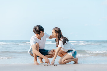 Romantic couple draw heart shapes in the sand on the beach.