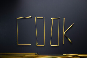Word 'COOK' written with spaghetti on gray background, top view, copy space. Food supplies, food donation on quarantine while coronavirus.