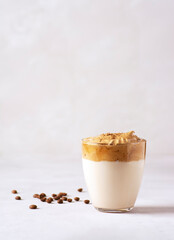 Dalgona coffee, a trendy drink. Dalgona coffee stands in a glass on a gray concrete table, next to it are coffee beans. Vertical orientation, there is a copy space.