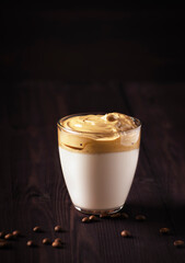 Dalgona coffee, a trendy drink. Dalgona coffee stands in a glass on a dark wooden table, next - coffee beans. Vertical orientation, there is a place for copying.