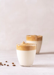 Dalgona coffee, a trendy drink. Two glasses of Dalgona coffee stand on a gray concrete table, with coffee beans nearby. Vertical orientation, there is a copy space.
