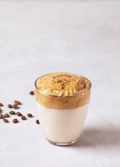 Dalgona coffee, a trendy drink. Dalgona coffee stands in a glass on a gray concrete table, next to it are coffee beans. Vertical orientation, there is a copy space.