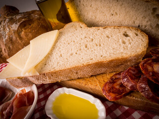 rebanadas grandes de pan payes hogaza con decoración de embutidos  chorizo y jamón con aceite de oliva sobre mantel de cuadros 