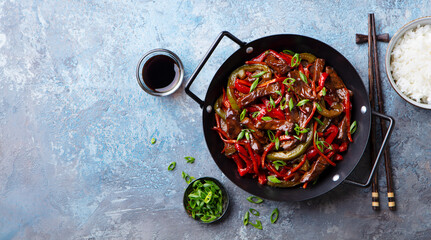 Beef and vegetables stir fry in a pan and rice. Blue stone background. Copy space. Top view.