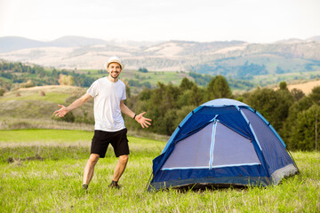 Young man with hands up camping tent facing amazing views of mountain