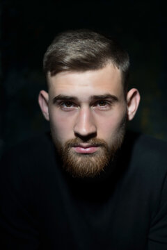 portrait of a bearded eared young guy of twenty-five years old, in black clothes, on a dark background. Studio portrait on black