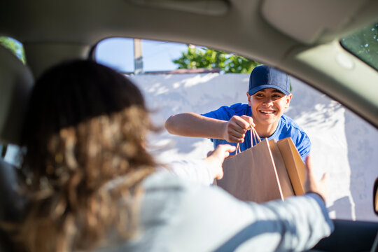 Joven trabajador de restaurante entregando comida en bolsas de cart&oacute;n a la cliente en su coche