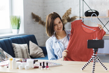 Young beautiful woman blogger showing clothes at camera, recording a tutorial video for her fashion...