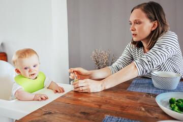 Young woman feeding baby daughter with puree. Little girl having meal with her mother in dining...