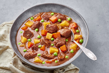 Irish Beef Stew in matt gray bowl on concrete background. Stew with beef or lamb meat with potatoes, carrots, peas and herbs. Traditional american and european food. Dinner mear