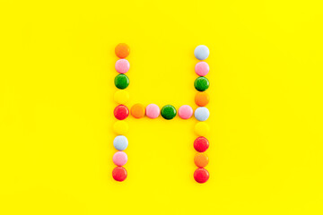 Letter H - alphabet made with sweets on yellow from above