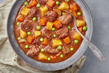 Irish Beef Stew in matt gray bowl on concrete background. Stew with beef or lamb meat with potatoes, carrots, peas and herbs. Traditional american and european food. Dinner mear