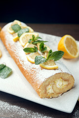 Lemon roll cake decorated with slices of lemon fruit and leaves of mint