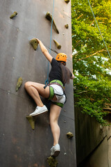 Woman in shorts and black shirt with safety equipment climbing an artifical climbing wall.