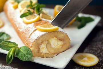 Lemon roll cake decorated with slices of lemon fruit and leaves of mint