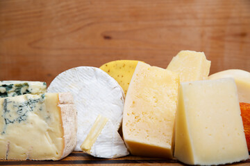 Closeup of various cheeses laying on wooden board. Edam, gouda, cheddar. Studio shot. Side view. Dairy meal and cooking on isolation concept for flyers and banners