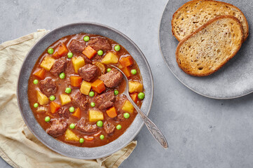 Irish Beef Stew with bread in matt gray bowl on concrete background. Stew with beef or lamb meat with potatoes, carrots, peas and herbs. Traditional american and european food. Dinner meal