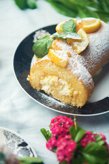 A piece of lemon roll cake decorated with slices of lemon fruit and leaves of mint