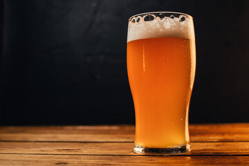 Glass of cold pale beer placed on a rustic wooden table