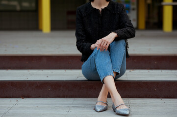 Fashionable young woman wearing flat silver shoes, blue jeans and black tweed jacket on the city...