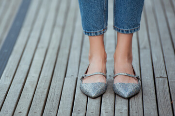 Fashionable young woman in silver shine flat shoes and blue jeans on the city street. Street style.