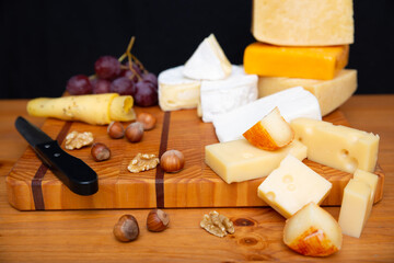 Different cheeses, grapes and nuts laying on wooden board. Parmesan, edam, gouda. Studio shot. Selective focus. Side view. Dairy meal and cooking on isolation concept for flyers and banners