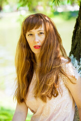 Naklejka premium Portrait of a young beautiful redhair girl on the background of tree bark