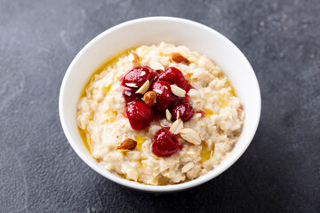 Oatmeal porridge with strawberry jam in white bowl. Grey background. Close up.