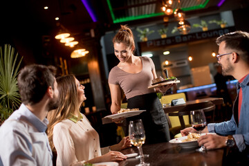 Waiter woman serving group of friends with food in the restaurant