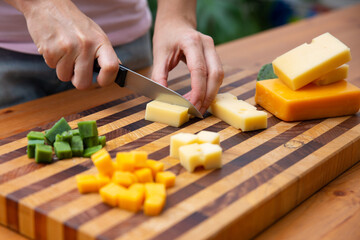 Obraz premium Woman cutting cheese on dices with knife. Edam, gouda, cheddar. Studio shot. Side view. Dairy meal and cooking on isolation concept for flyers and banners