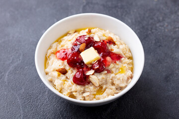 Oatmeal porridge with butter and strawberry jam in white bowl. Grey background. Close up.