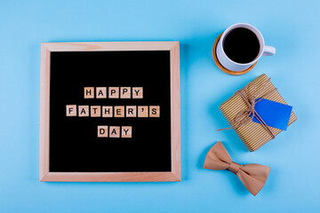 Obraz na płótnie Canvas Letters board, cup of coffee, gift with empty blank and bowtie on blue background. Top view in flat lay style. Happy Fathers Day Concept.