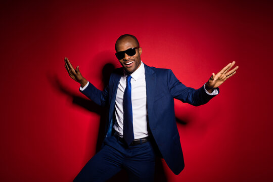 Photo of handsome dark skin business boss guy chilling resting corporate party event raise hands dancing star wear sun specs formalwear suit tuxedo isolated red burgundy background