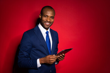 Portrait of his he nice attractive cheerful guy investor holding in hands ebook reading stock exchange world finance news isolated over red maroon burgundy marsala color background