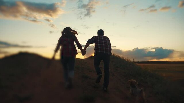 happy family couple and dog runs hands jumping up for joy at sunset on a hilltop and jumps. concept of team business concept travel freedom victory happiness teamwork. happy family parents hold hands