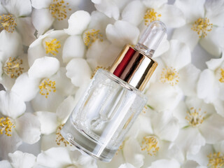 bottle with cosmetic serum on a background of jasmine flowers. Jasmine essential oil