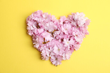 Heart made with sakura blossom on yellow background, top view. Japanese cherry