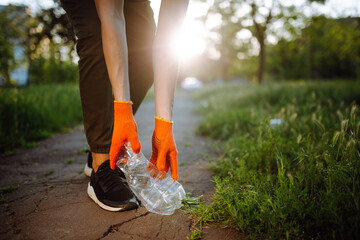 Young man volunteer picks up trash at the park. Plastic bottle is being collected by the man...