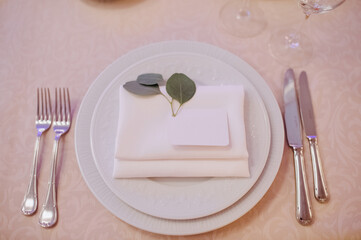 Restaurant, banquet, table setting. The table is covered with a white tablecloth, dishes, white clean plates, cutlery, napkins, wine glasses, candles. Close-up.