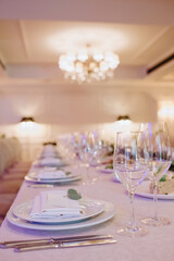 Restaurant, banquet, table setting. The table is covered with a white tablecloth, dishes, white clean plates, cutlery, napkins, wine glasses, candles. Close-up.