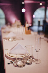 Restaurant, banquet, table setting. The table is covered with a white tablecloth, dishes, white clean plates, cutlery, napkins, wine glasses, candles. Close-up.
