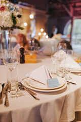 Restaurant, banquet, table setting. The table is covered with a white tablecloth, dishes, white clean plates, cutlery, napkins, wine glasses, candles. Close-up.