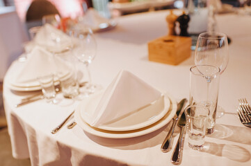 Restaurant, banquet, table setting. The table is covered with a white tablecloth, dishes, white clean plates, cutlery, napkins, wine glasses, candles. Close-up.