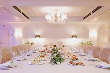 Restaurant, banquet, table setting. The table is covered with a white tablecloth, dishes, white clean plates, cutlery, napkins, wine glasses, candles. Close-up.